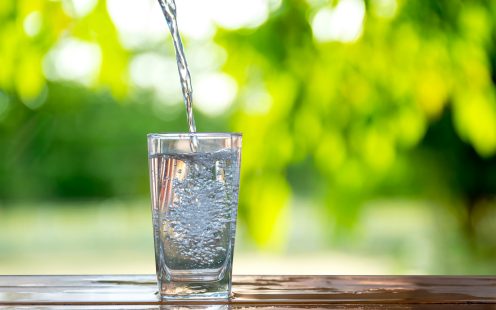 Water flows into a glass placed on a wooden bar.