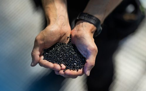 Nærbilde av hender som holder en håndfull små sorte plastgranulater.