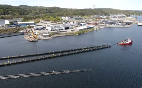 En rød båt sleper lange rør bak seg.