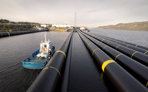 A blue boat drives along long lengths of black pipes